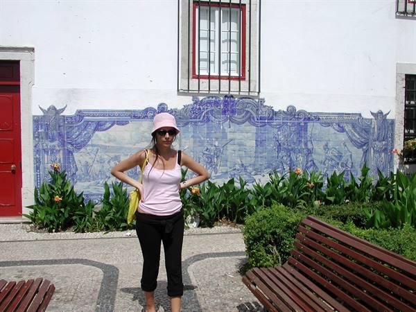 Woman in pink hat posing in front of blue azulejo panels on a white wall