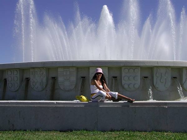 Woman seated before Madrid's monumental fountain, water jets in sunlight