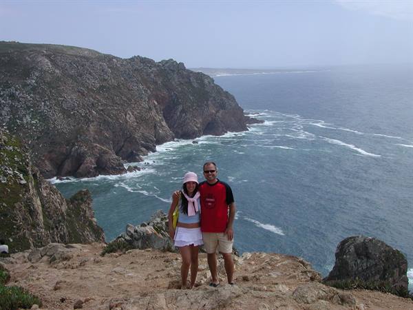 Couple posing on rocky cliff above the ocean, white waves among rocks, Cabo da Roca
