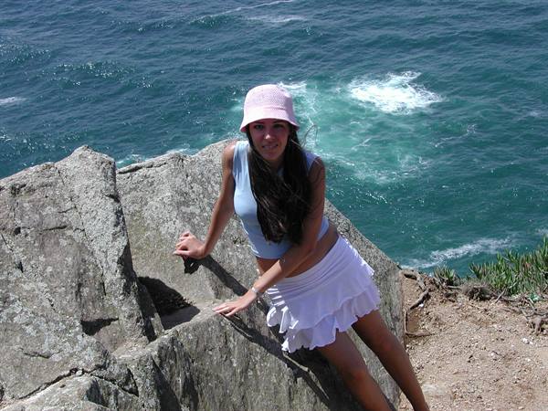 Girl in pink hat leaning on gray rocks above turquoise sea