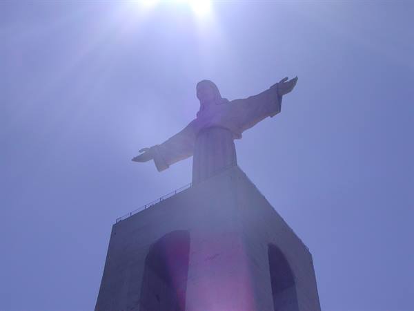 Christ the King statue with open arms against the sun, blue sky
