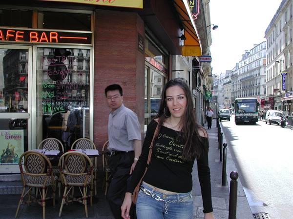 Woman on a city street outside a café bar with wicker chairs, bus approaching