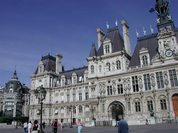 Tourists walk in front of the stone facade of the Hôtel de Ville, Paris