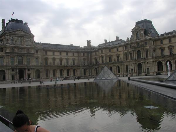 Glass pyramid and reflecting pool in the Louvre courtyard under cloudy sky