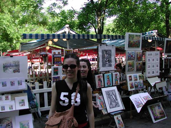 Young woman in black shirt and sunglasses among open-air painters' stalls