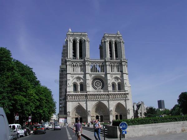 Tourists walk in front of Notre-Dame's Gothic facade in Paris under blue sky