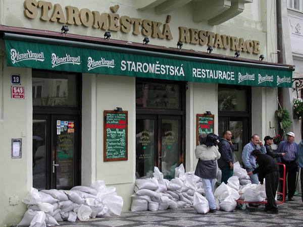 Sandbags piled outside Staroměstská Restaurace, people loading more with a trolley