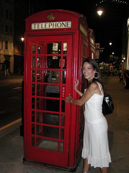 Woman in white dress beside a red telephone booth in London at night