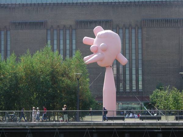 Pink inflatable sculpture outside Tate Modern, people strolling along the Thames