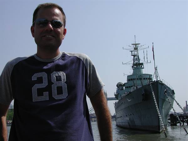 Man wearing number 28 shirt in front of HMS Belfast cruiser on the Thames
