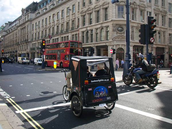 Pedal rickshaw crossing Oxford Street junction with red double-decker buses