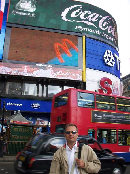 Tourist in sunglasses before red double-decker and Piccadilly Circus billboards