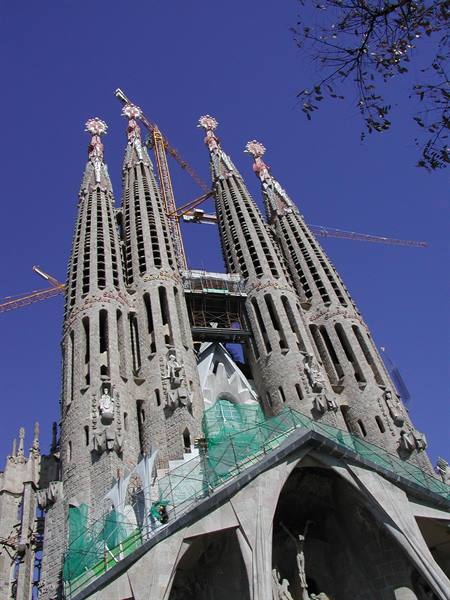 The spires of Sagrada Família in Barcelona with cranes and scaffolding under blue sky
