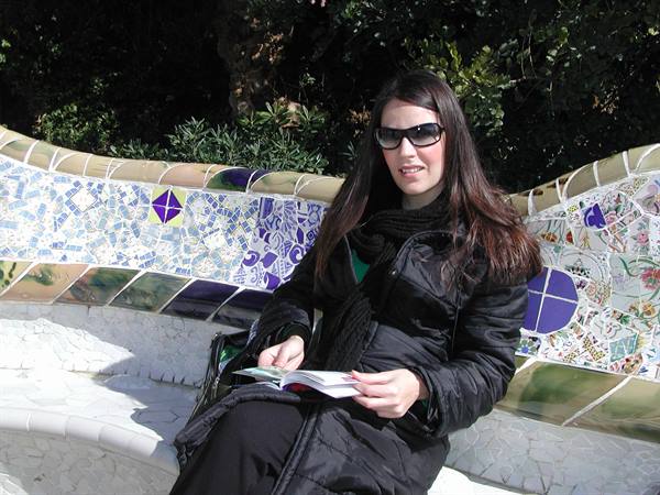 Woman sitting on Gaudí's mosaic bench at Park Güell, reading a guidebook