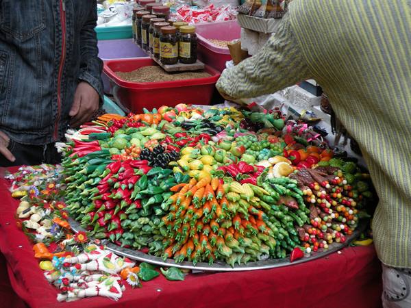 Vendor at market stall with marzipan fruits and vegetables on tray