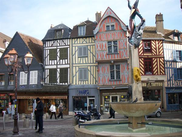 Fountain before colorful half-timbered houses in Troyes, pedestrians and scooters in the square