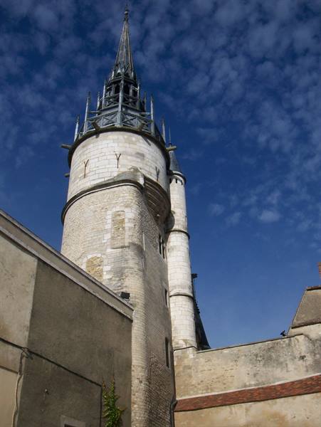 Stone tower with openwork spire rising above rooftops, blue sky