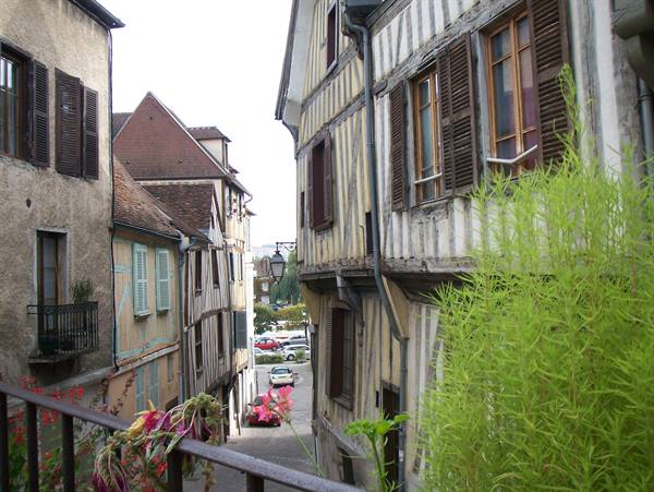 Narrow lane between half-timbered houses, flowers on the railing, cars below