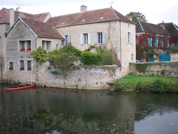 Stone houses with shutters by the river, a red rowboat moored under grey sky