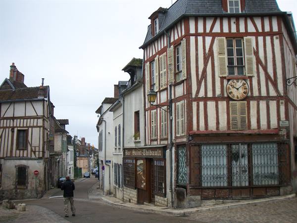 Half-timbered houses with clock in Auxerre street, a man walks under grey sky