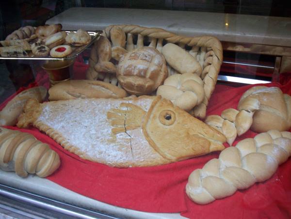 Fish-shaped and braided breads in a bakery window, dusted with powdered sugar