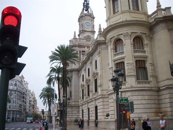 Red traffic light in front of Valencia town hall with palm trees and pedestrians