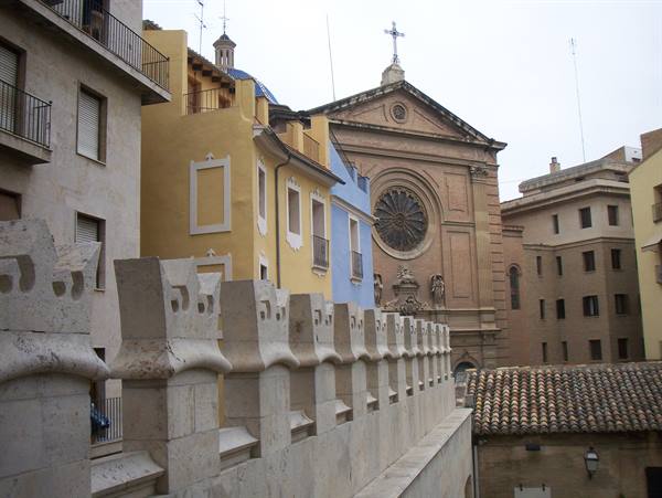 Stone battlements in front of yellow houses and a rose-window church, Valencia