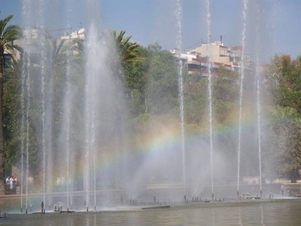 Fountain jets create a rainbow above the green pond
