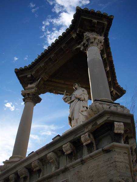 Stone saint statue under a columned shrine against the blue sky