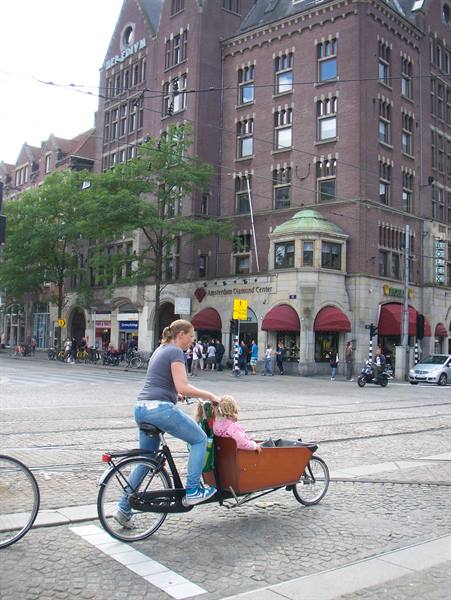 Woman rides cargo bike with child past shops in Amsterdam