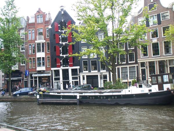 Houseboat moored on an Amsterdam canal with brick facades and green trees