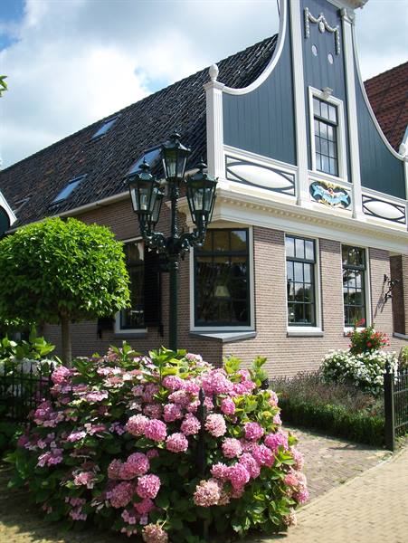 Brick facade with green wooden gable, wrought-iron lampposts and pink hydrangeas