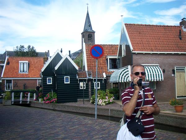 Tourist with camcorder among green wooden houses and tiled roofs, church tower behind
