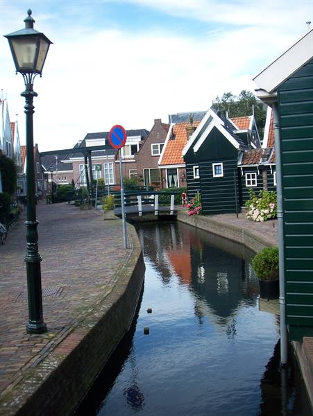 Canal between green wooden houses, brick pavement, lamppost and drawbridge in Volendam
