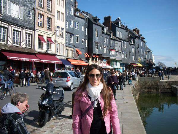 Woman in pink jacket and white scarf at Honfleur harbor among slate houses and cafés