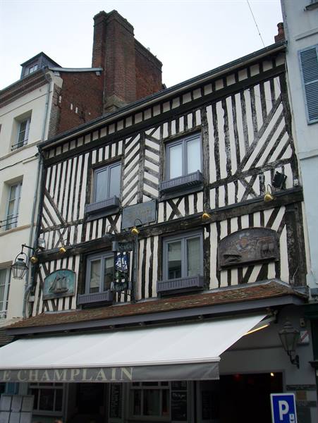 Half-timbered facade of Le Champlain restaurant in Honfleur, under grey sky