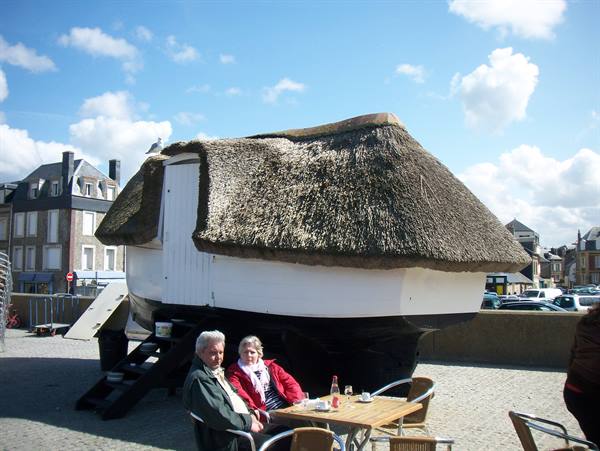 Couple sipping coffee in front of a thatched-roof boat on a square