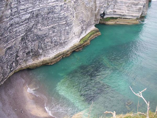 Limestone cliffs of Étretat above turquoise water and small pebble beach