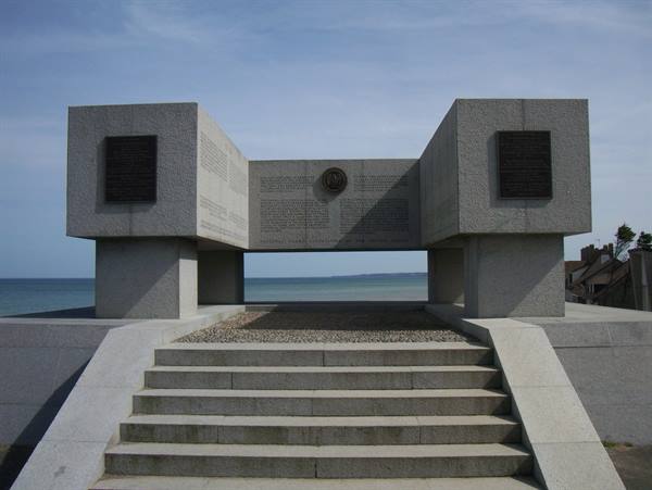 Concrete monument with bronze plaques on Omaha Beach under clear sky