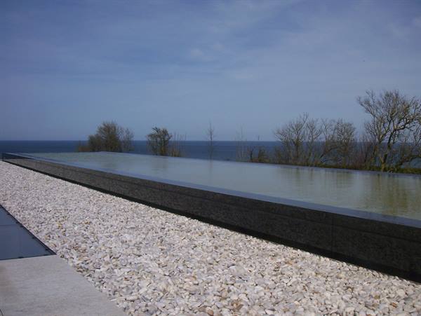 Black stone water pool with white gravel, bare trees and the sea