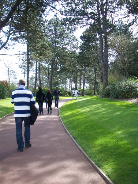 People strolling on a curving path among pine trees and green lawn