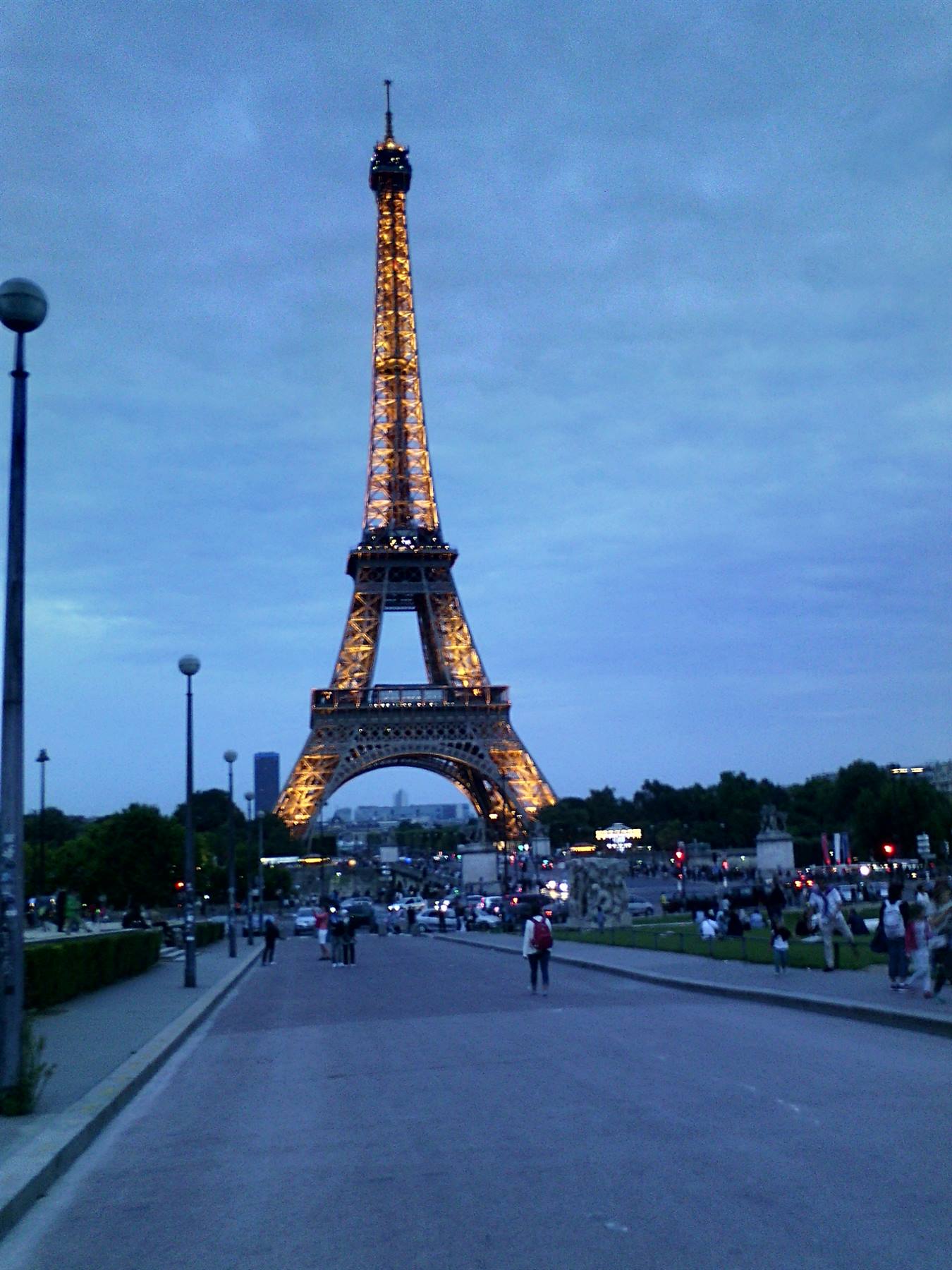 Torre Eiffel illuminata al crepuscolo, gente passeggia along Champ de Mars