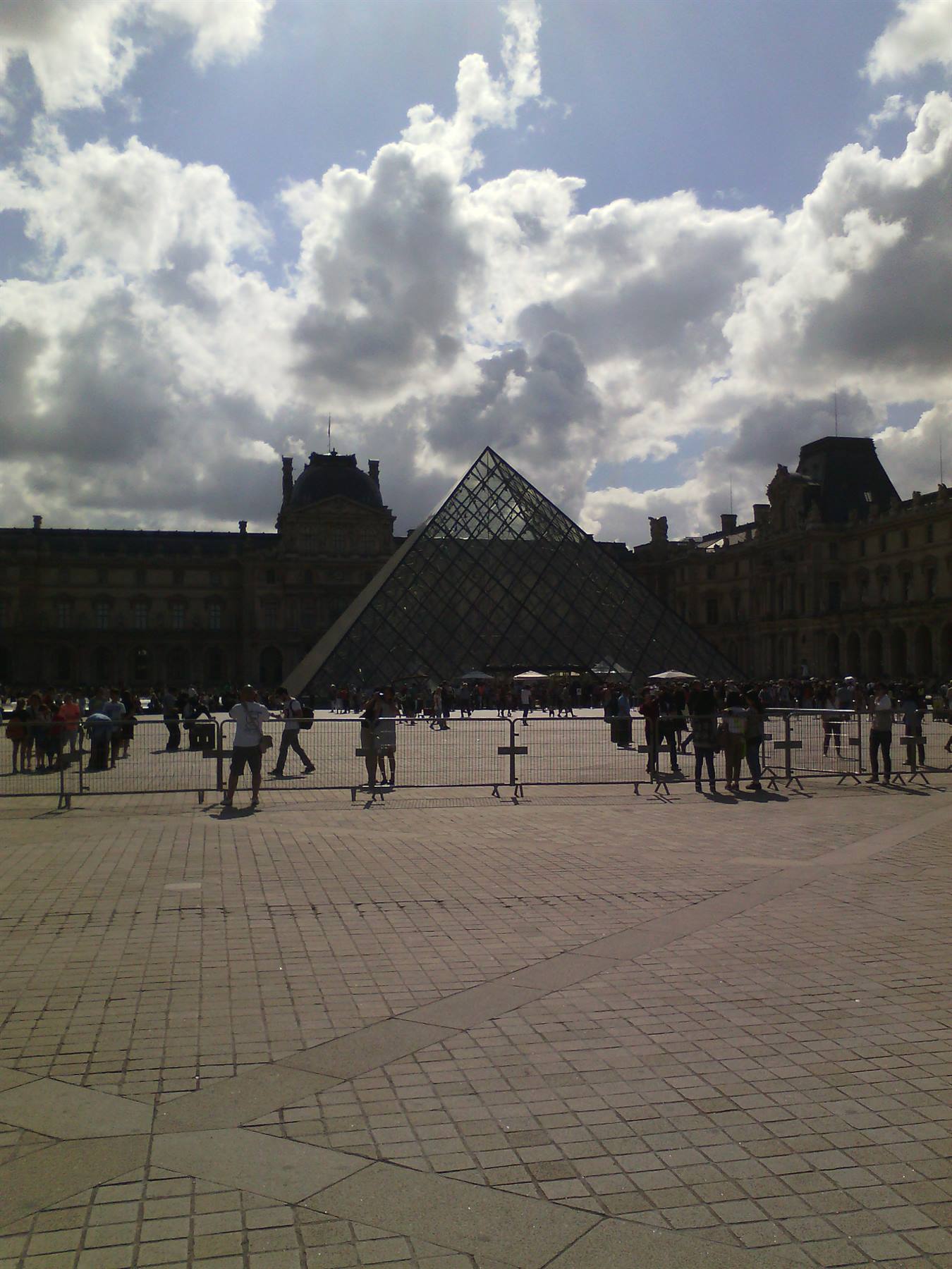 Piramide di vetro del Louvre tra nuvole, turisti nella corte di Parigi