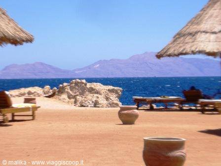 Sandy beach with straw umbrellas, wooden loungers and mountains across the sea