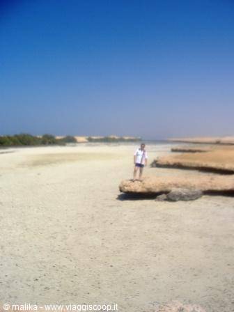 Woman standing on a flat rock, sandy beach, clear blue sky
