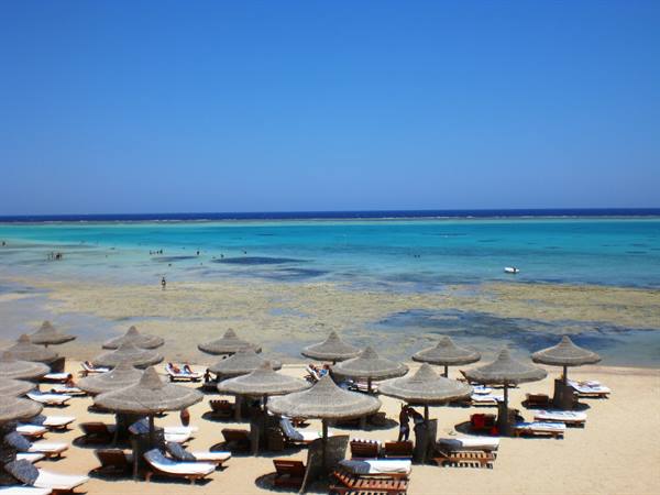 Straw umbrellas and sun loungers on a beach, turquoise water with swimmers