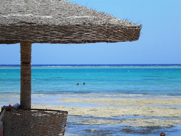Straw beach umbrella over turquoise sea with swimmers in shallow water