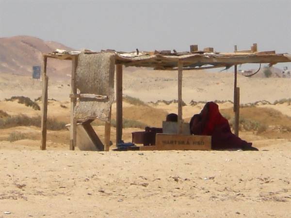 Woman in red veil under a wooden shack in the sandy desert