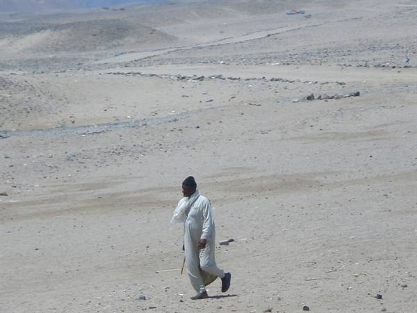 Man in white robe walking across the rocky desert sand