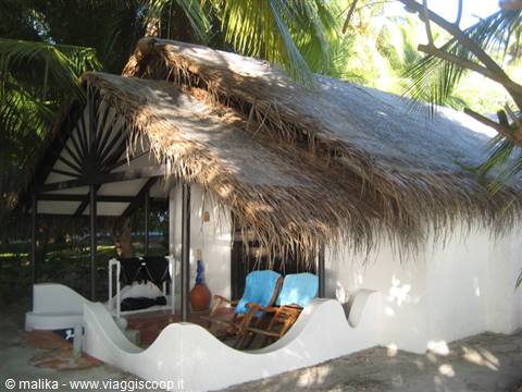 Thatched-roof bungalow with blue deck chairs among palm trees